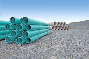 Stacked PVC water pipe and concrete storm sewer pipe on a new road construction site.